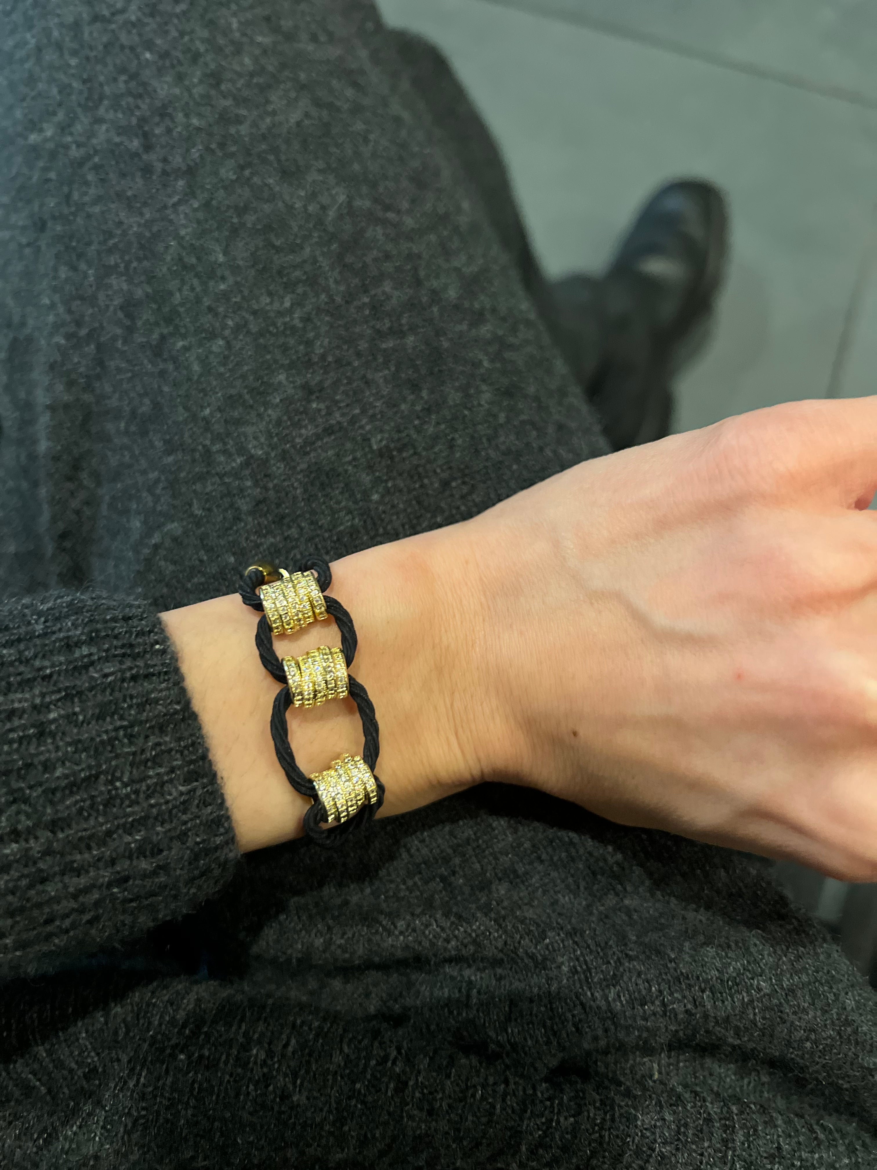 Jeweled hair tie gold plated with CZ and black cord worn as bracelet against dark sweater.