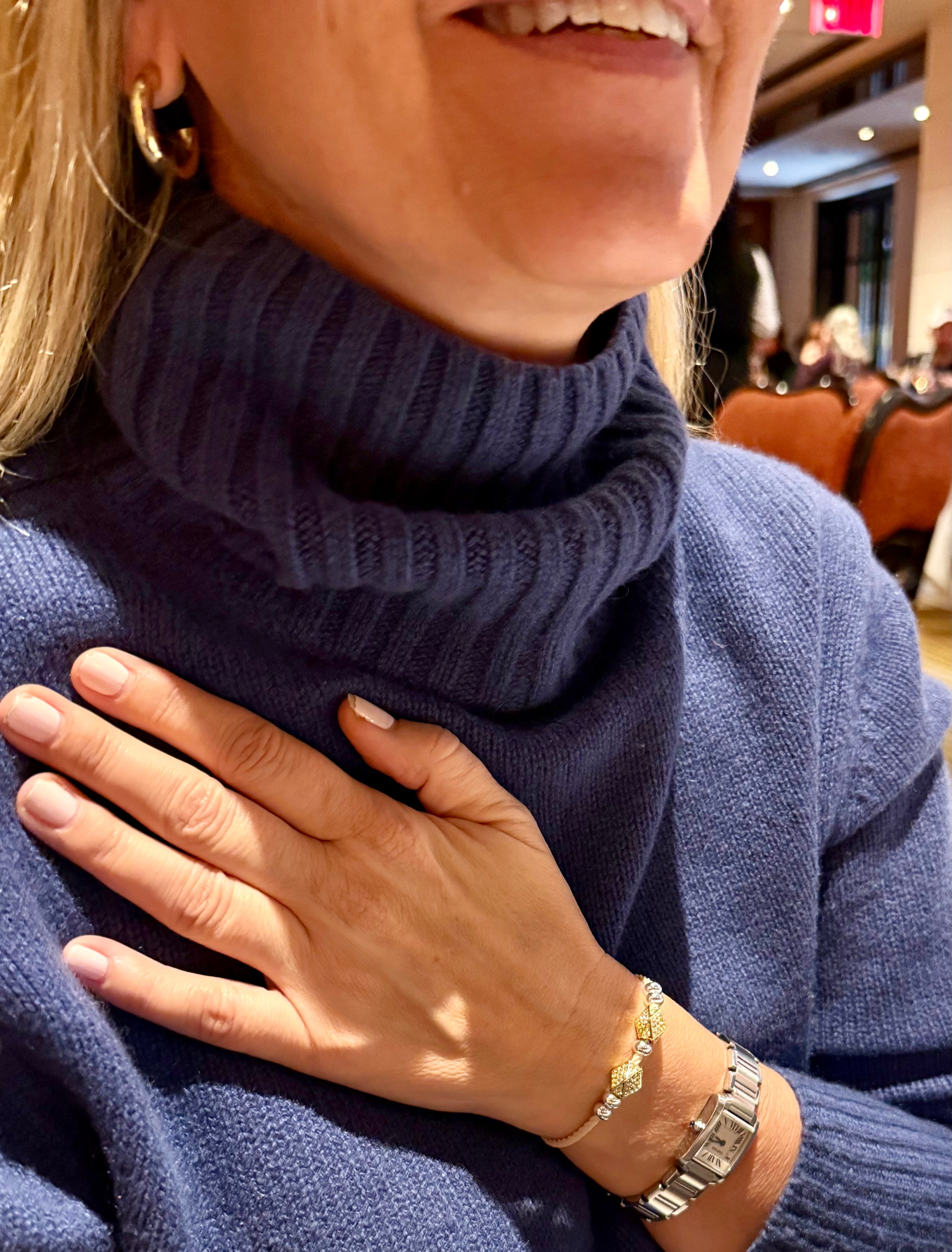 Blonde woman wearing a blue turtleneck sweater with jeweled hair tie gold plated, CZ on light beige cord