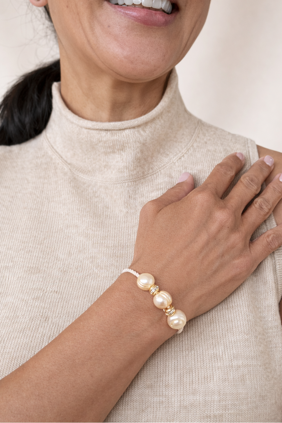 Woman wearing a pearl jeweled hair tie as bracelet on a neutral background